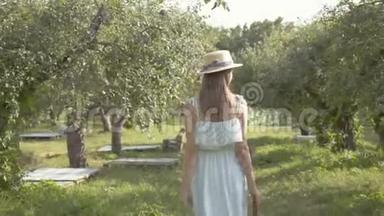 漂亮的年轻女子戴着草帽，穿着长长的白色连衣裙穿过绿色的夏天花园。 免费<strong>农村生活</strong>