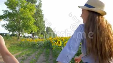戴着草帽的快乐女朋友手牵着手走在田野上，带着黄色的向日葵在户外散步