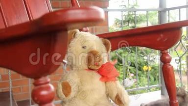 一只老式玩具熊坐在一个开放的阳台上的摇椅上摇摆。 夏季蔬菜。