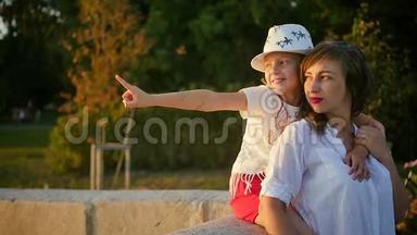 妈妈在她女儿旁边欣赏城市日落。 戴着可爱帽子的可爱的母女被<strong>傍晚</strong>的<strong>阳光</strong>照亮