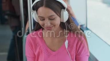 坐在公共交通工具上享受旅行的年轻女乘客，戴着耳机坐在现代有轨电车的车窗旁。