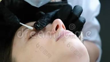 美容师用棉签擦拭病人`眼睑。 睫毛层压板。 特写眼睛。