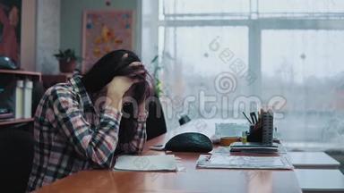 年轻的黑发女人坐在一张桌子前，<strong>惊慌失措</strong>，头痛。