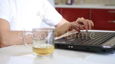 一个女孩的手在<strong>笔记本</strong>电脑<strong>键盘</strong>上打字。 <strong>笔记本</strong>电脑旁边是一杯茶。