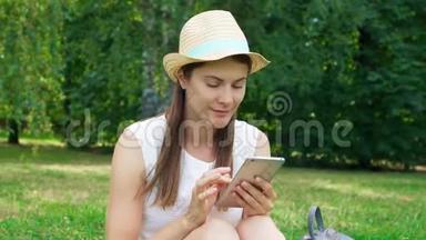 女学生用手机坐在大学校园的草地上。 公共公园的游客用手机聊天