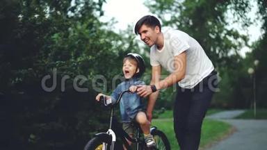 快乐的年轻人爱<strong>父亲</strong>的慢动作在夏天的绿色公园里<strong>教孩子</strong>骑自行车，小男孩在笑
