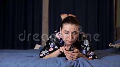 美丽的黑发女孩躺在床上用手机。 网上约会