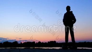 黎明时分，一个少年骑着一个两轮自平衡气垫船装置，沿着河堤靠近池塘。 生活方式。 Silhou