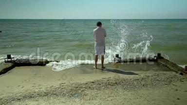 一个年轻人站在海滩上看着<strong>海浪</strong>。 <strong>海浪</strong>拍打着海岸. 慢动作。