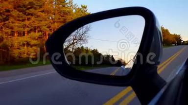 日落时驾驶乡村道路侧镜。 司机视角POV向下看侧视镜沿街道近黄昏