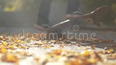 玩滑板的家伙的腿特写。 公脚滑板在公园的落叶上..