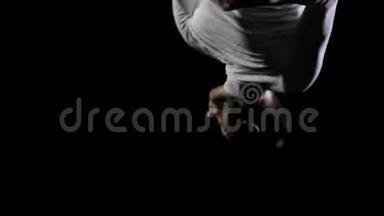 年轻英俊的男杂技演员穿着白色衣服在黑色背景下做跳跃和展示旋转技巧