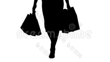 剪影让`去购物吧！ 漂亮的女人带着购物袋走路的腿。