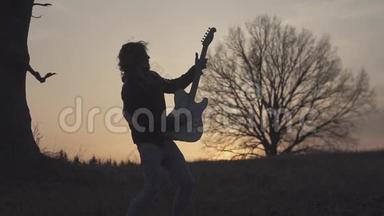 日落时分，人们在靠近树的田野里弹着电吉他，唱歌。 剪影