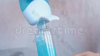 女人`手在一小瓶大瓶子里倒入蓝色的淋浴凝胶。 旅行的罐子。 瓶子特写。