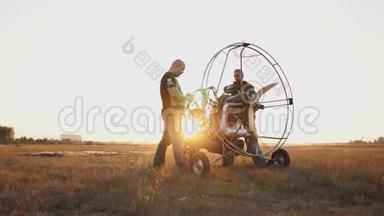 汽车<strong>滑翔伞</strong>在日落时用一个木制螺旋桨站在一片田野里，两名飞行员在飞行前热身发动机。 A.