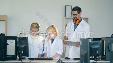 一个十几岁的男孩和一个女孩正和一个研究人员一起看着一台<strong>电脑显示器</strong>