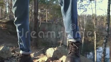 穿着<strong>靴子</strong>和蓝色牛仔裤的男腿站在悬崖边的岩石上。 山区<strong>靴子</strong>的绿景