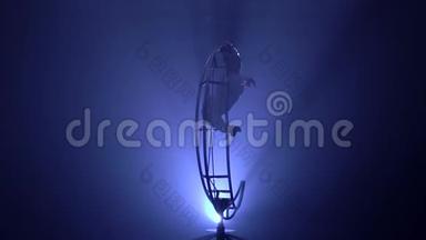 体操运动员倒挂在旋转结构的月亮上的一根绳子上。 蓝色烟雾背景。 慢<strong>动作</strong>。 <strong>剪影</strong>