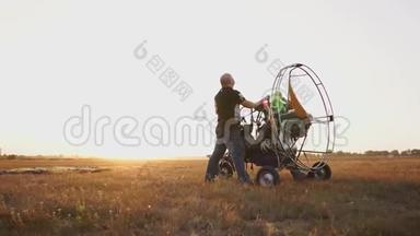 汽车<strong>滑翔伞</strong>在日落时分用一个木制螺旋桨站在田野里，两名飞行员对发动机进行了一次试车