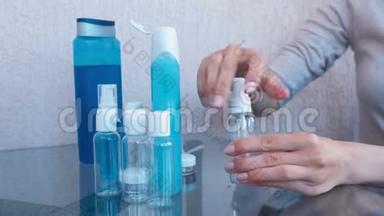 女人`手在一小瓶大瓶子里倒入蓝色的淋浴凝胶。 旅行的罐子。