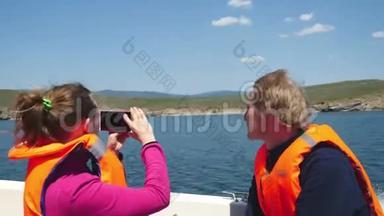 年轻夫妇穿着救生衣乘船游湖。 女孩用手机拍照。 3840x2160