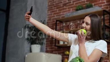 女人在家厨房用<strong>手机浏览</strong>。 年轻女子在智能手机上浏览，微笑着快乐。 女人吃苹果