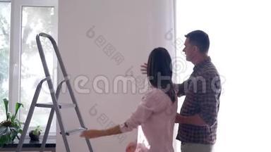 美丽的夫妇做翻新和使用阶梯悬挂图片在白色墙壁在平面