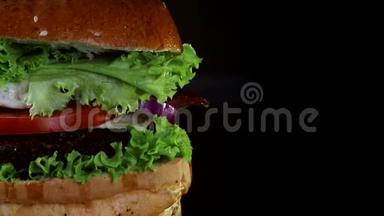 汉堡，有一个切块和炒鸡蛋覆盖绿色旋转在木板上。 从黑色的背景。