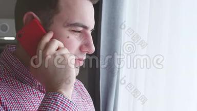 穿着格子衬衫的年轻人一边看着窗外一边用红色手机说话。 4K. 库存情况