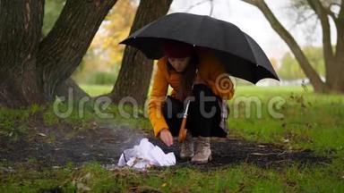 女人在多风的秋天公园里试着在雨中<strong>生火</strong>