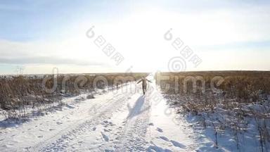 一个年轻的女孩欢快地走着，跳上一片白雪覆盖的田野。 冬天阳光明媚的欢乐景象，有一条路和一片雪域
