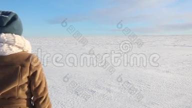 一个年轻的女孩欢快地走着，跳上一片白雪覆盖的田野。 冬天阳光明媚的欢乐景象，有一条路和一片雪域