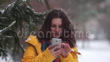 一个卷曲的黑发<strong>女孩</strong>在一场<strong>雪中</strong>带着智能手机在公园里散步的亲密肖像。 在<strong>雪</strong>的背景下
