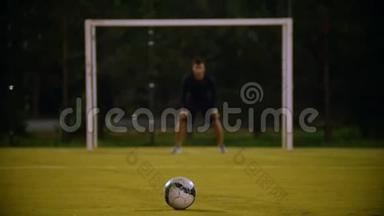 球落在前景的草地上，守门员在门口，另一个球员踢球，但球确实如此
