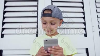 戴着帽子和t恤的孩子正拿着一部智能手机在他面前，集中精力在一个白色的电子游戏上