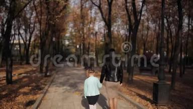 妈妈和女儿正沿着一条布满秋黄树叶的大道走着。 一家人在城市<strong>公园散步</strong>