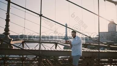 快乐的白种人独自站在布鲁克林<strong>大</strong>桥上，在阳光明媚的<strong>夏日</strong>里，一边看一边使用智能手表手镯