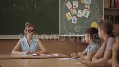 女老师在小朋友面前.. 教室里的漂亮老师坐在桌子前问孩子们。 教育