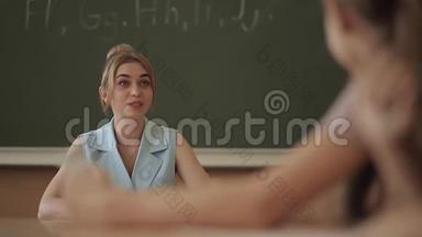 女老师在小朋友面前.. 教室里的漂亮老师坐在桌子前问孩子们。 教育