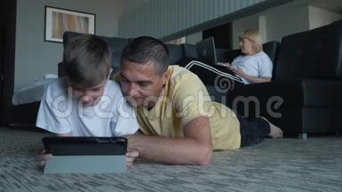 一个幸福的家庭，一个孩子躺在地毯上，使用数字平板电脑和智能手<strong>机</strong>。 现代技术