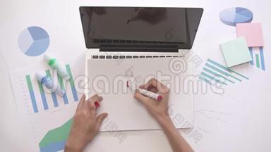 女人在笔记本电脑上的一张纸上写工作。 带有图表的业务桌面。