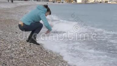 孤独寒冷海滩的女人。 白种人女人从迎面而来的海浪中<strong>跳出</strong>来，在水面上玩石头