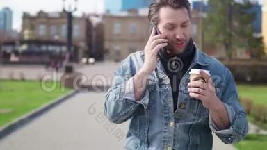 在大城市的人行道上行走的有魅力的大胡子男人。 会说话的手机。 喝着美味的咖啡。 现代和现代