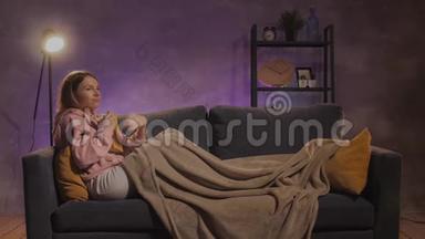 一个年轻的女人坐在沙发上看书。 女孩在温暖的房间里的舒适沙发上做梦