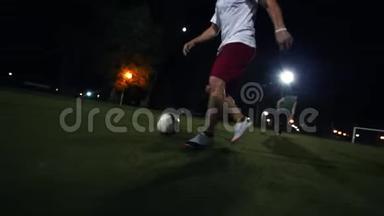 穿着勃艮第短裤和白色运动鞋的年轻人在绿野上领球，夜间射击