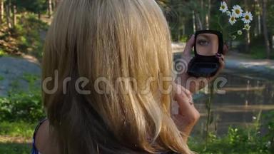 夏季公园化妆品粉和照镜子的金发女人