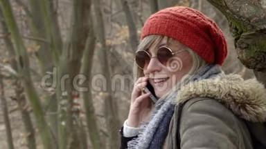 年轻漂亮的女人，戴着红帽子坐在树旁，用手机说话