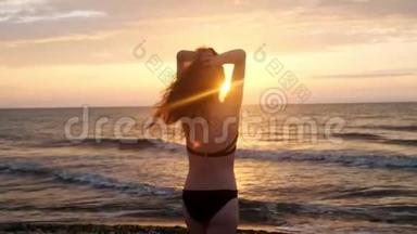 穿黑色泳衣的时髦女孩在日落时进入大海。 我对大海和海滩很满意。 关于