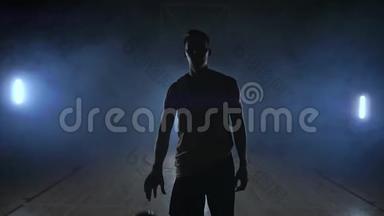 篮球运动员在一个黑暗的房间里径直走向<strong>摄像机</strong>，烟雾中有一个背光的背部看着<strong>摄像机</strong>。